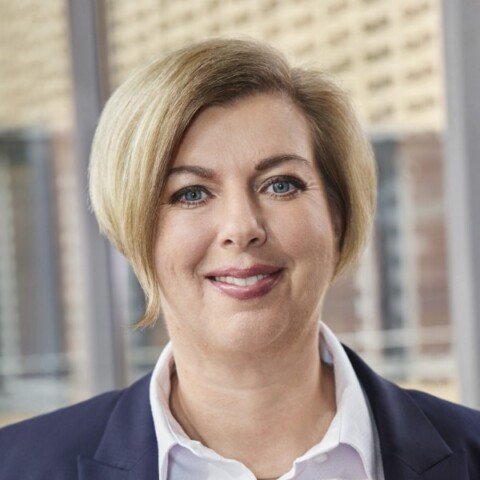 Headshot portrait of Karin Thelen, Managing Director of Stadtwerke München, standing in front of an office building.