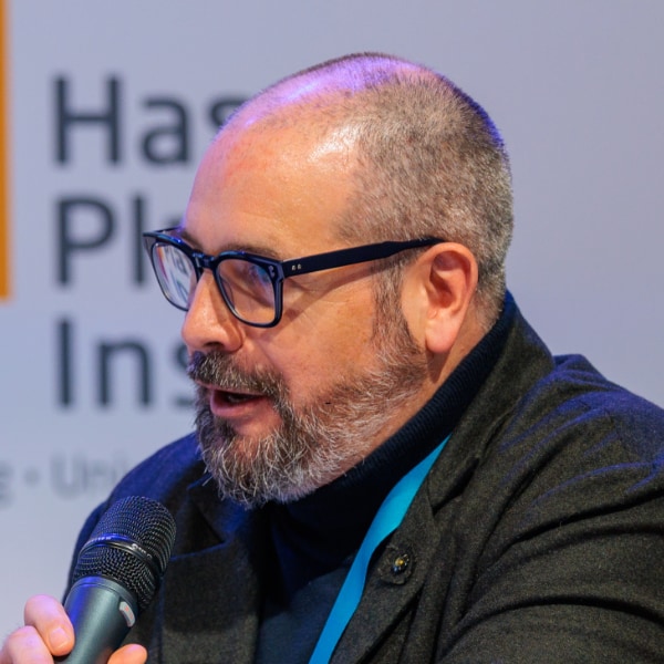 Digital health expert Nick Schneider, holding a microphone, speaking at a conference, looking left outside of the frame.