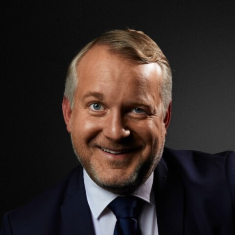 Studio headshot portrait of Thomas Girst, Global Head of Cultural Engagement for the BMW Group, brightly lit in front of a dark background.
