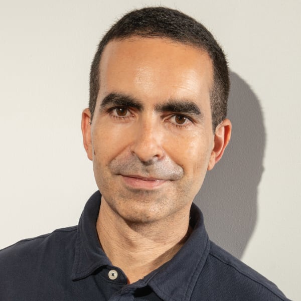 Headshot portrait of InstaDeep co-founder Karim Beguir in front of a neutral grey wall, casting a visible shadow.