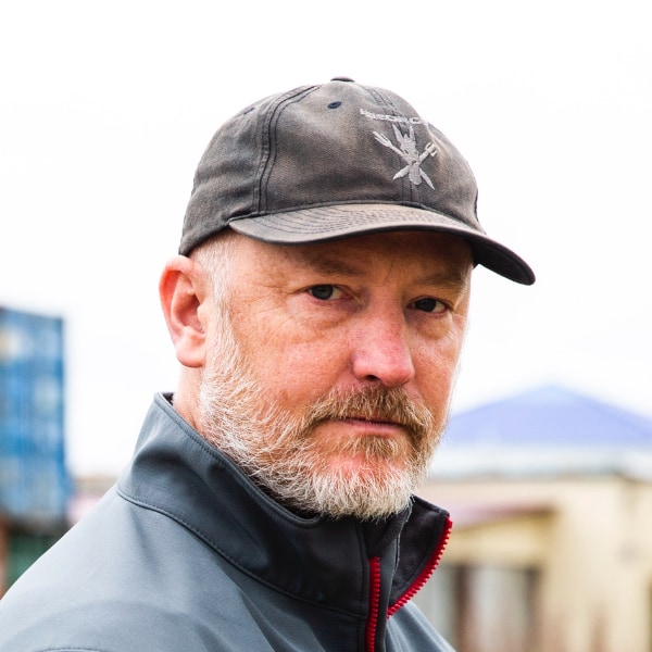 Environmental portrait of Alexander Rose, formerly with the Long Now Foundation, now with Automattic, wearing a black outdoor jacket and black baseball cap, looking at the camera.