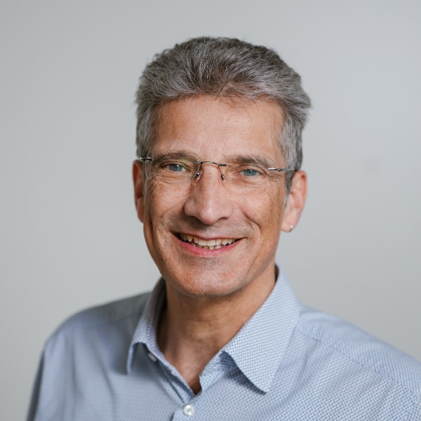 Headshot portrait of German AI expert Antonio Krüger in front of a light grey studio background, smiling at the camera.