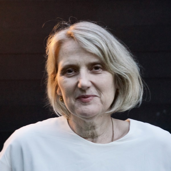 Headshot portrait of Crunchbase analyst Gené Teare, wearing a white shirt in front of a dark background, smiling at the camera.