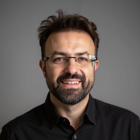 Studio portrait of AI and robotics expert Mirko Holzer, SPRIND, in front of a grey background, smiling at the camera.
