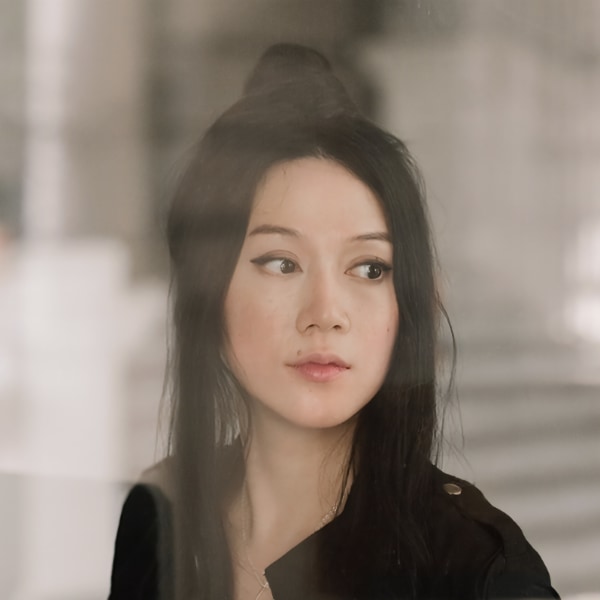 Artistic headshot portrait of artist Sougwen Chung, looking over her left shoulder, seen through glass or a layer of a milky filter effect.