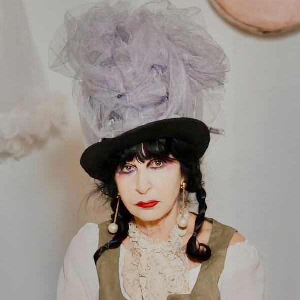 Staged portrait of artist Colette Lumiere, wearing a costume and big hat, looking sad