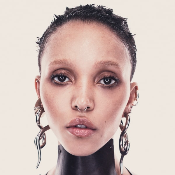 Studio portrait of artist FKA twigs by photographer Jordan Hemingway, showing her straight at the camera in front of a beige-grey background.