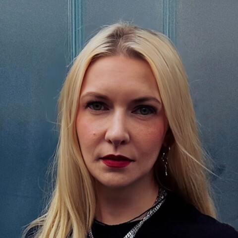 Dark, underexposed headshot portrait of Franziska Gregor, Serviceplan Group, standing in front of a blue background.