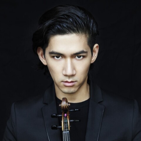 Portrait of musician Iskandar Widjaja in front of a black studio background, holding a violin, looking straight at the camera.