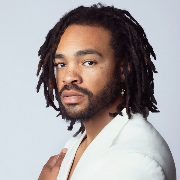 Headshot portrait of musician and producer Maejor, seen in front of a grey studio background, looking at the camera.