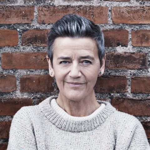 Former EU Commissioner Margrethe Vestager standing in front of a red brick wall.