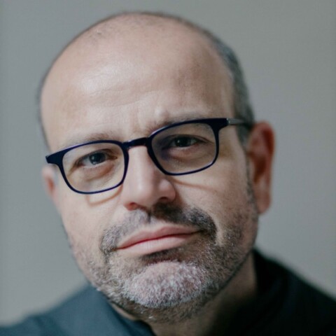 Close-up headshot portrait of Paolo Benanti, Catholic priest and professor at LUISS Guido Carli University in Rome, seen in front of a grey studio background.