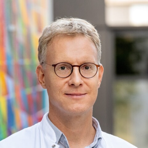 Portrait of neurologist Prof. Simon Jacob, TUM, in front of a wall with a colorful pattern.