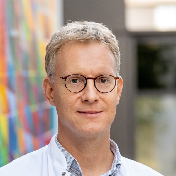 Portrait of neurologist Prof. Simon Jacob, TUM, in front of a wall with a colorful pattern.