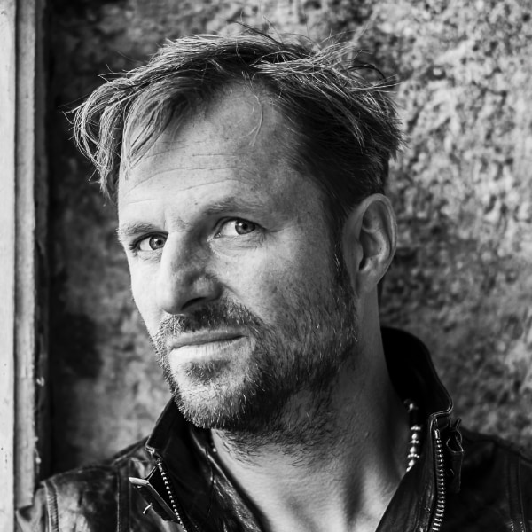 Black-and-white portrait of Austrian actor Philipp Hochmair, standing in front of a wall. Image credit: Stephan Brückler