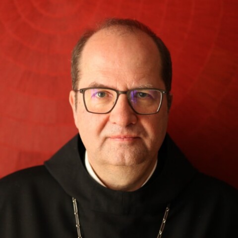 Headshot portrait of Abbot Jeremias Schröder, seen in front of a dark red studio background