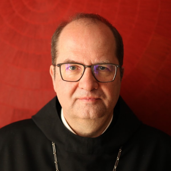 Headshot portrait of Abbot Jeremias Schröder, seen in front of a dark red studio background
