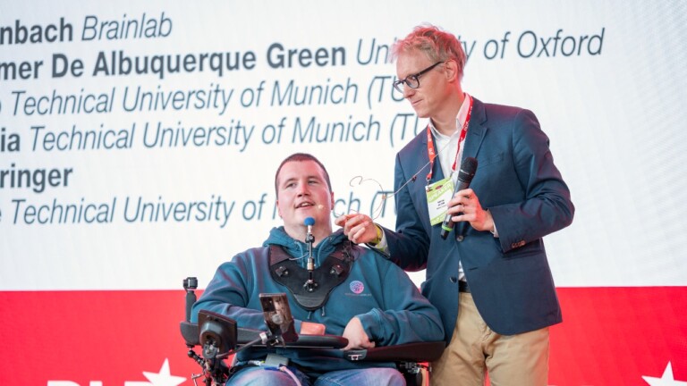 Michael (Michi) Mehringer, first person in Europe with tetraplegia to have a brain-computer interface implanted using microelectrodes, and Simon Jacob, TUM, on stage at the DLD Health x BAIOSPHERE in Munich, June 12, 2026. Photo: Philipp Guelland for DLD / Burda
