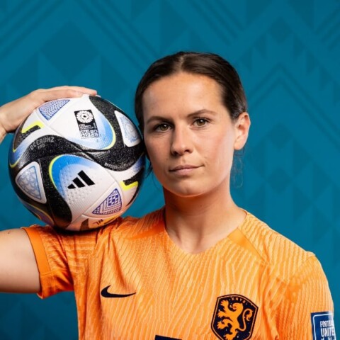 Studio portrait of football player Merel van Dongen holding a football, looking at the camera.