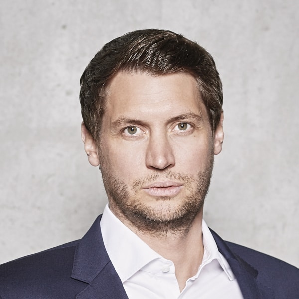 Headshot portrait of FC Bayern manager Thomas Ehemann, akak Tom Ehemann, in front of a grey wall.