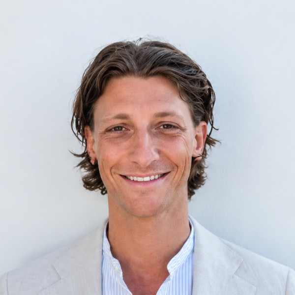 Headshot portrait of Yoran Henzler, co-founder of Entourage World, standing in front of a grey wall, smiling