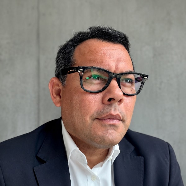 Headshot portrait of Krloos Rivera, Innsomnia Group, in front of a grey concrete wall