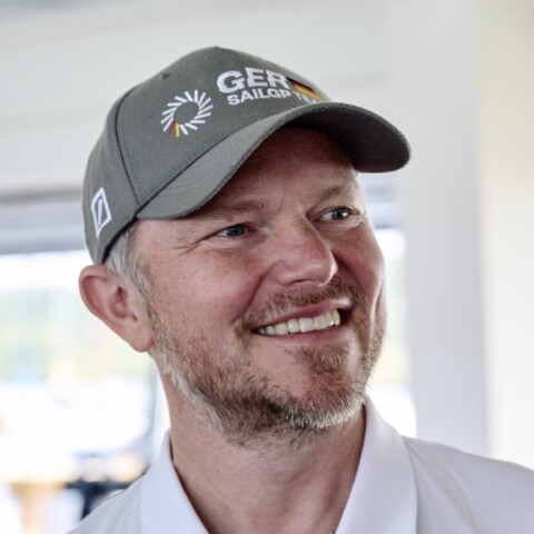 Environmental portrait of Tim Krieglstein, CEO of the Germany SailGP Team, smiling, looking to his left, wearing a baseball cap