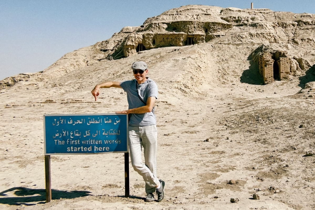 Author and professor of literature Martin Puchner seen in the desert of southern Iraq, near the town of Uruk. Puchner is pointing at a sign that reads, “The first written words started here”.