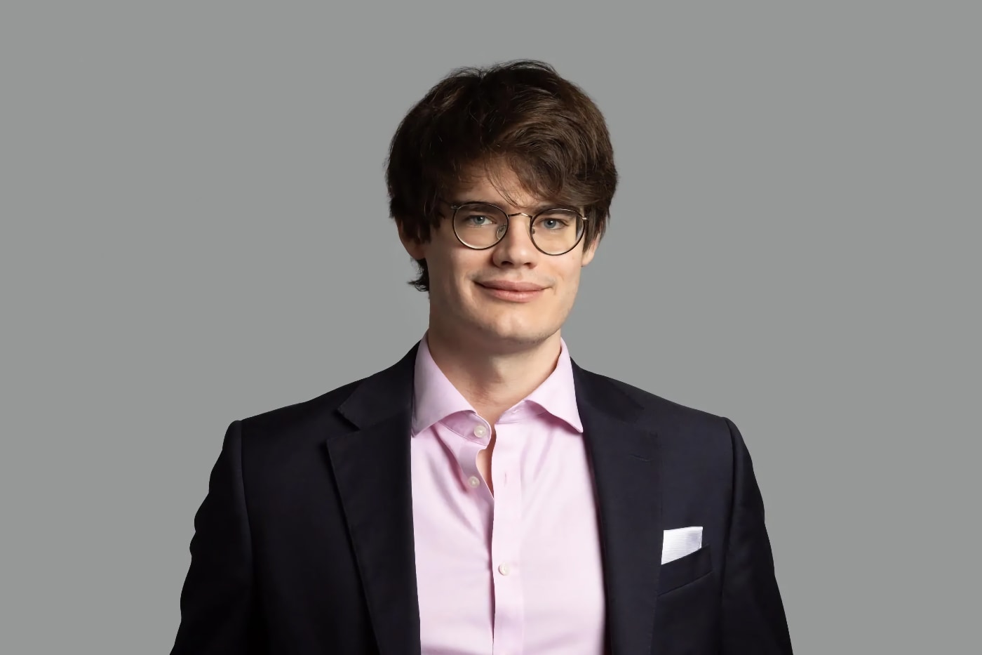 Studio portrait of Keegan McBride, Tony Blair Institute, standing in front of a grey background, wearing a suit.